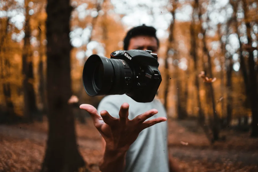 A photographer tossing a camera into the air in an autumn forest